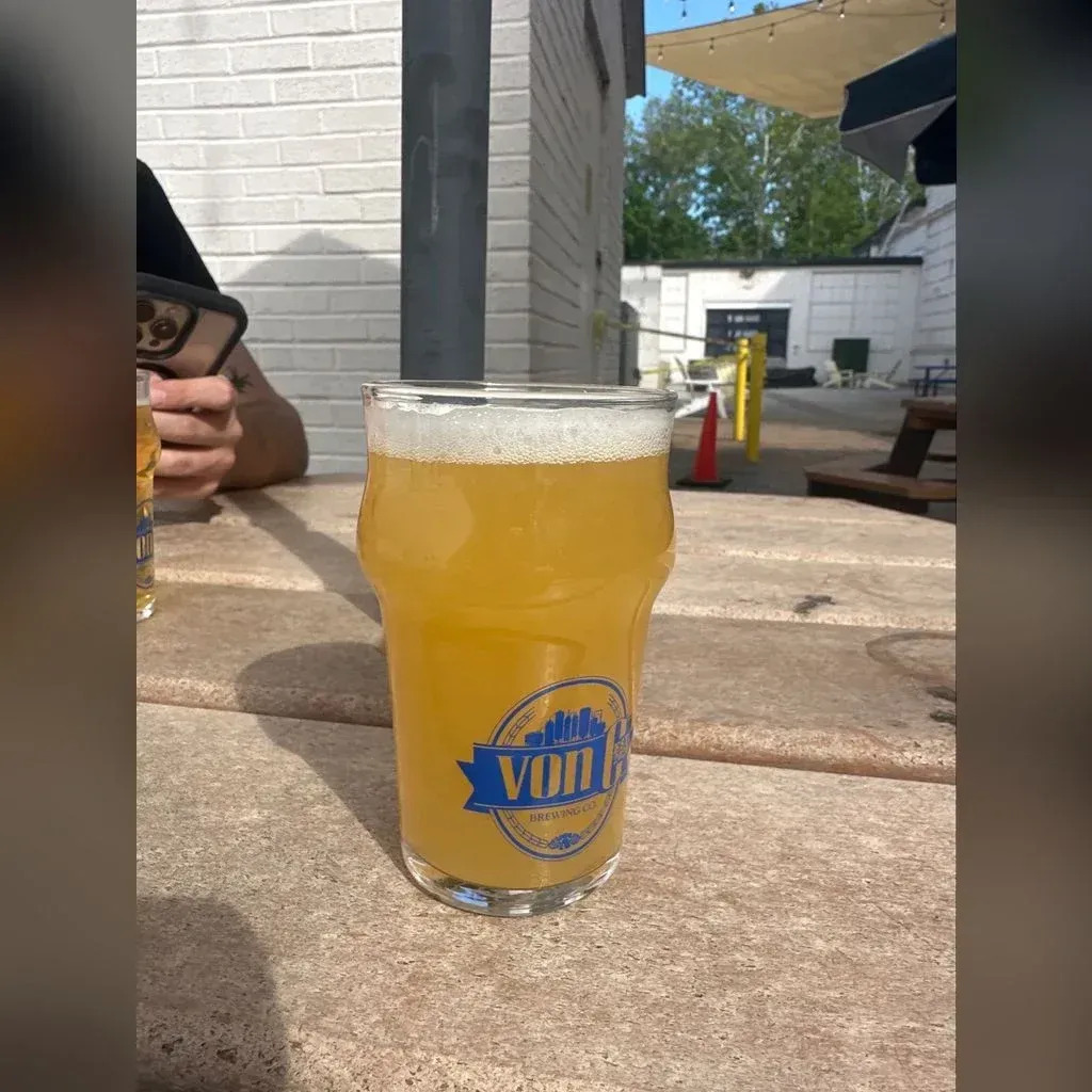 Hazy yellow Boundless Love NEIPA in a von C Brewing branded pint glass on a beer-garden table at the Norristown taproom, soft outdoor light catching the haze