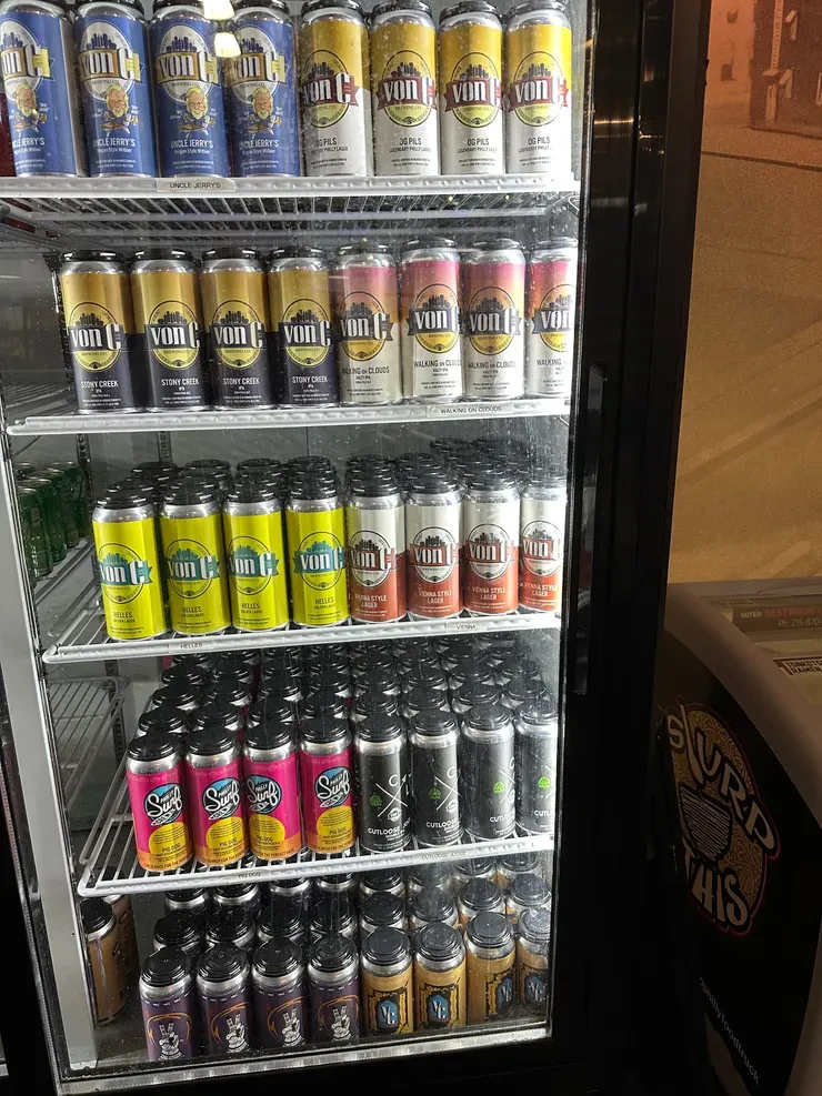 von C Brewing Co. retail cooler stocked with 16-oz 4-pack cans across the full lineup — Uncle Jerry's Wit, O.G. Pils, Walking on Clouds, Helles, Vienna Style Lager, Stony Creek IPA, Pig Dog Pale Ale, CutLoose Joose — the literal retail merchandising any bottle shop or grocery account can stage