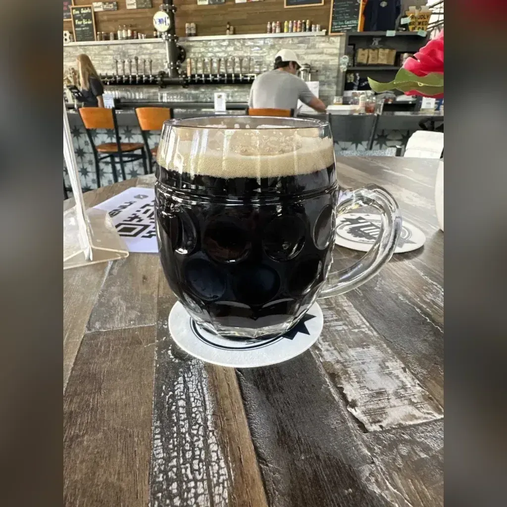 Czech-style dark lager Černé Speciál pour in a von C Brewing branded glass with a thick cream head, taproom interior softly behind