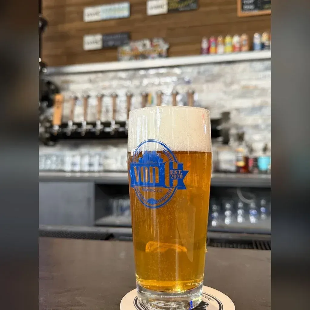 Pale gold Festbier in a tall von C Brewing branded pilsner glass on a coaster at the Norristown taproom bar, brass tap handles visible behind