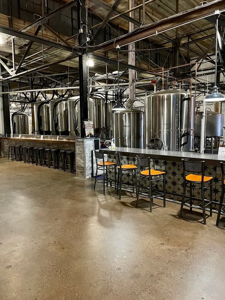 Stainless-steel fermentation tanks lined along the back wall of the von C Brewing Co. taproom in Norristown PA, bar stools at the foot of the tanks, polished concrete floor reflecting the warm overhead lights