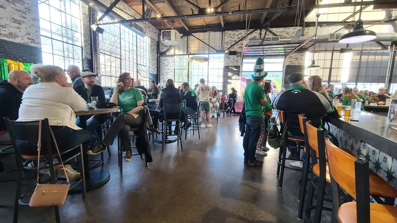 Packed taproom on a busy daytime — St Patrick's Day crowd with green attire — at von C Brewing in Norristown, exposed industrial ceilings and warm light