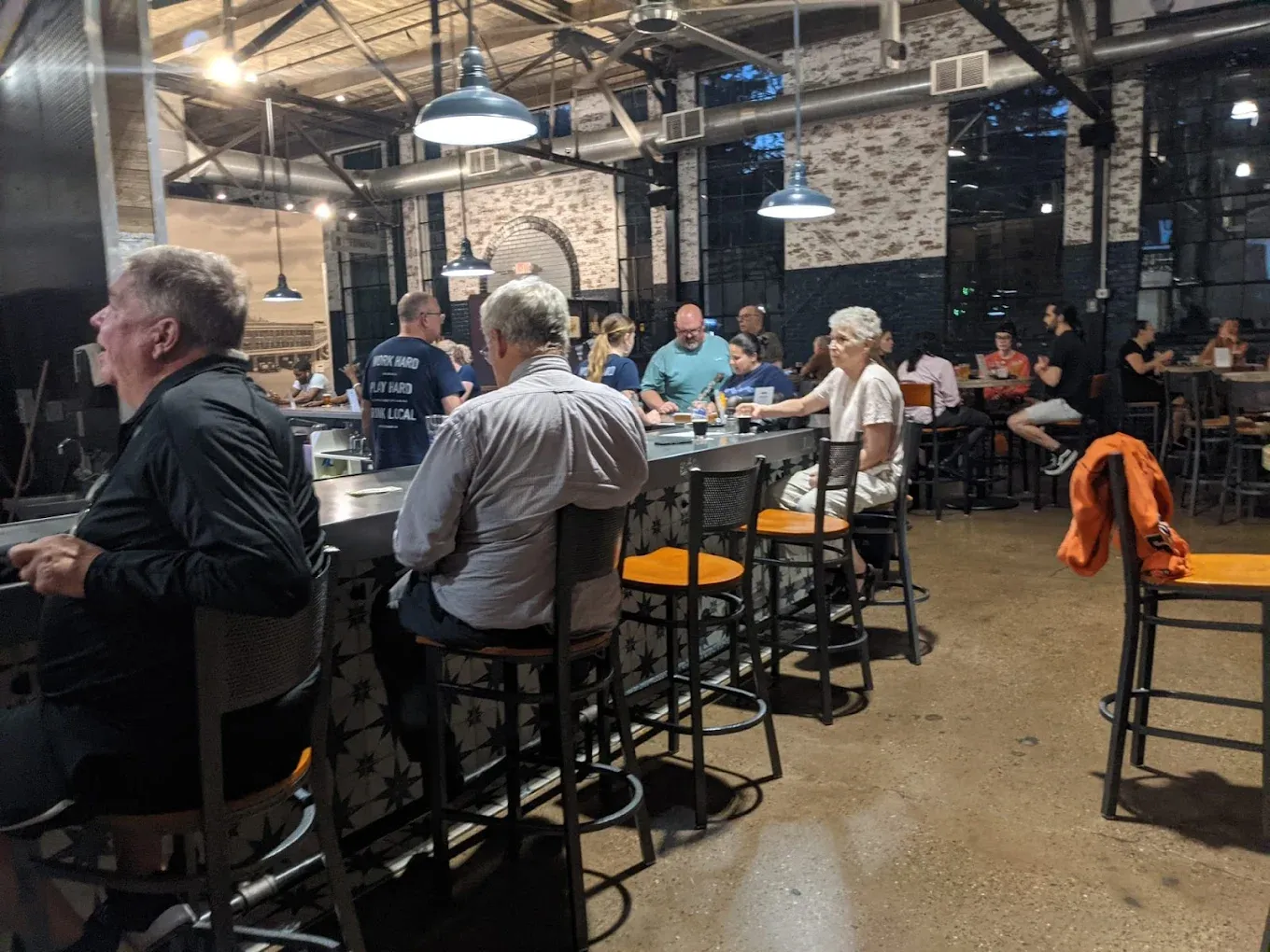 Intimate evening view of the von C Brewing bar with white brick wall, copper pendant lights overhead, patrons seated on bar stools enjoying pints in the converted-warehouse taproom