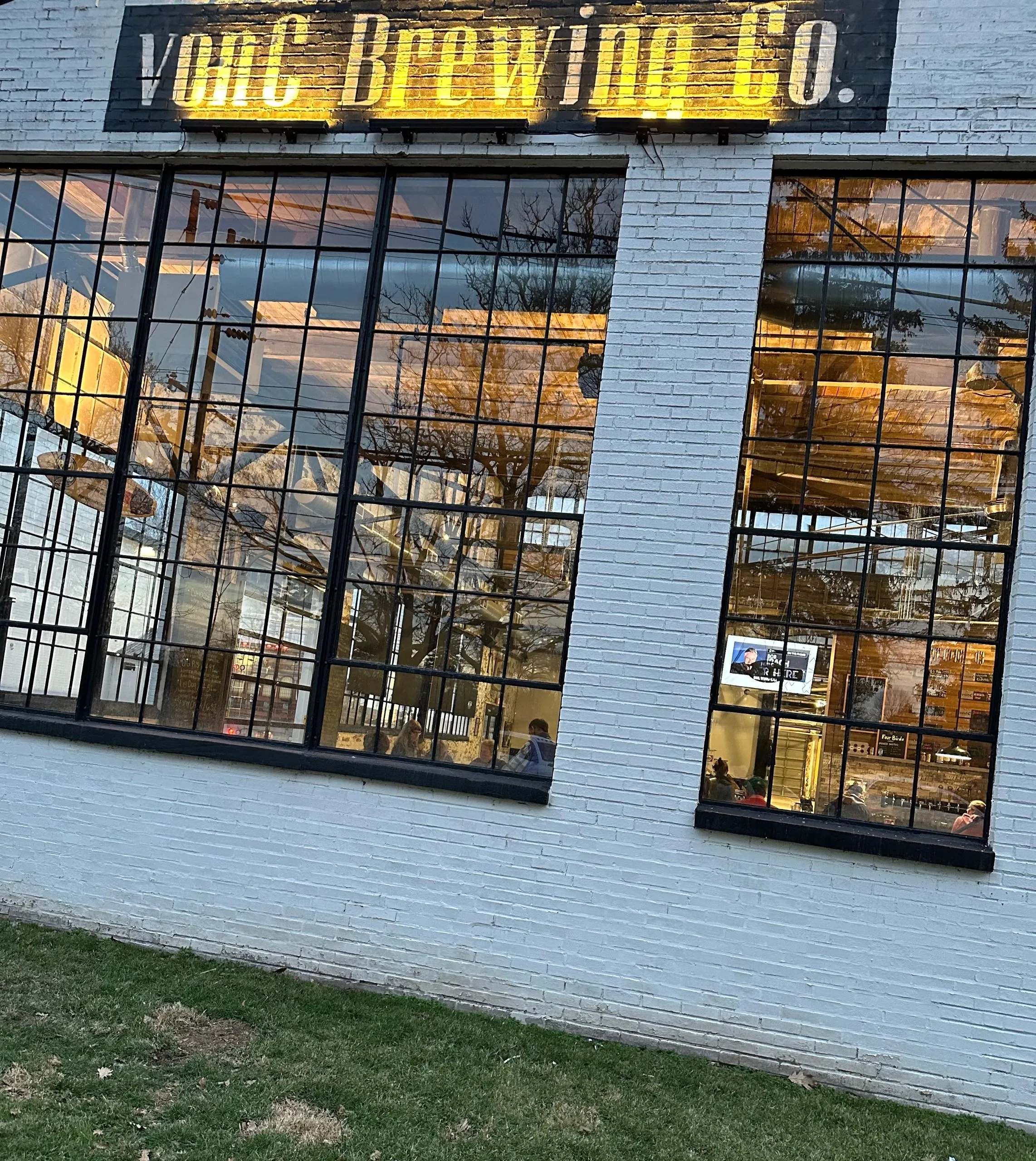 Illuminated von C Brewing Co. sign at dusk outside the reclaimed warehouse on Stanbridge Street in Norristown PA — warm amber glow against the early-evening sky