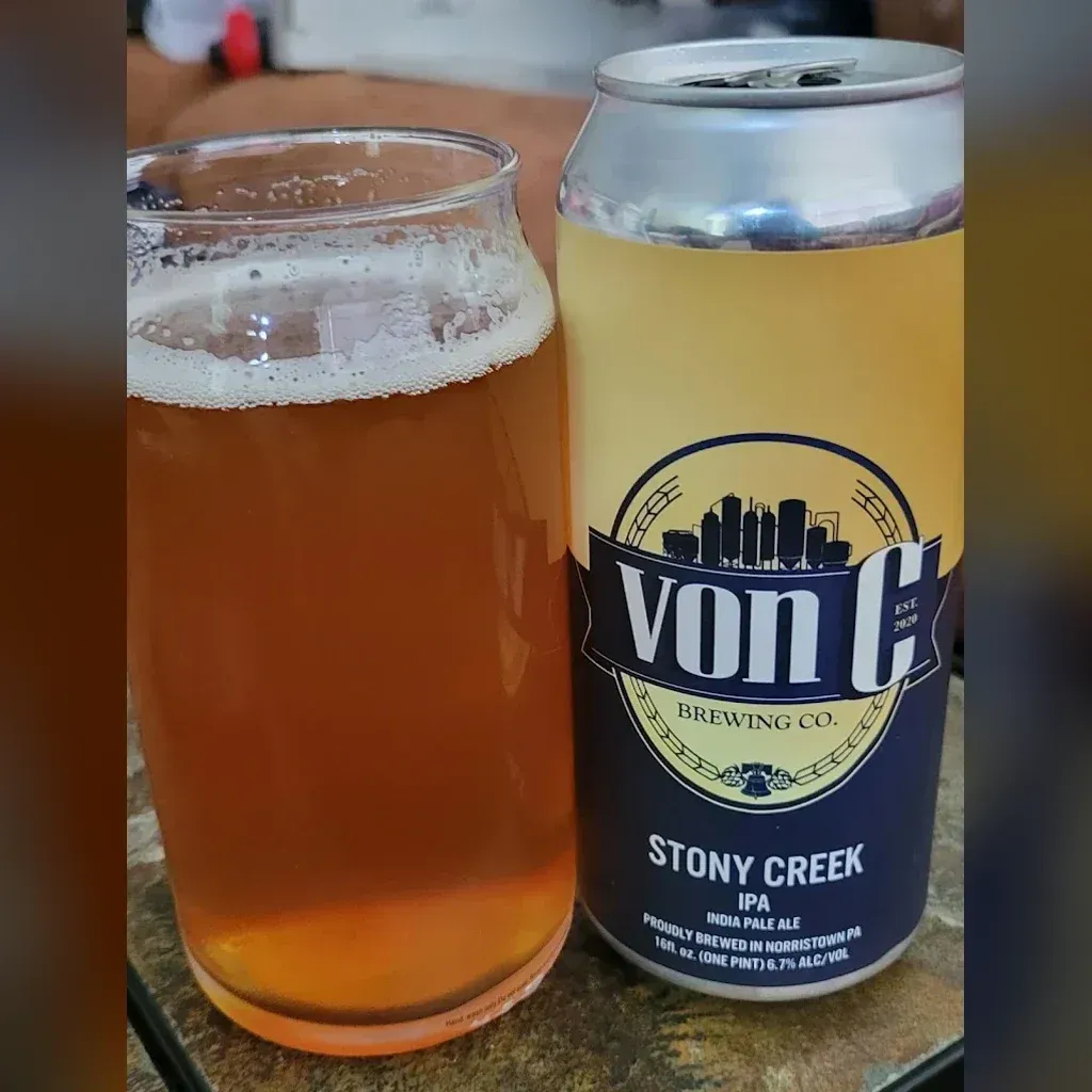 16 oz Stony Creek East Coast IPA can — von C Brewing wordmark, Norristown PA — beside a clear can-shaped glass with the freshly poured IPA on a stone bar top